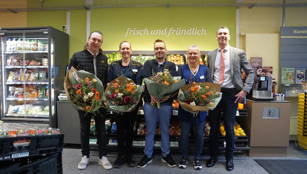 Fünf Personen, vier davon mit Blumenstrauss, posieren vor dem Gemüseregal eines Dorfladens für ein Foto.